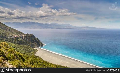 The black beach and village of Nonza on Cap Corse in Corsica with Desert des Agriates in the background