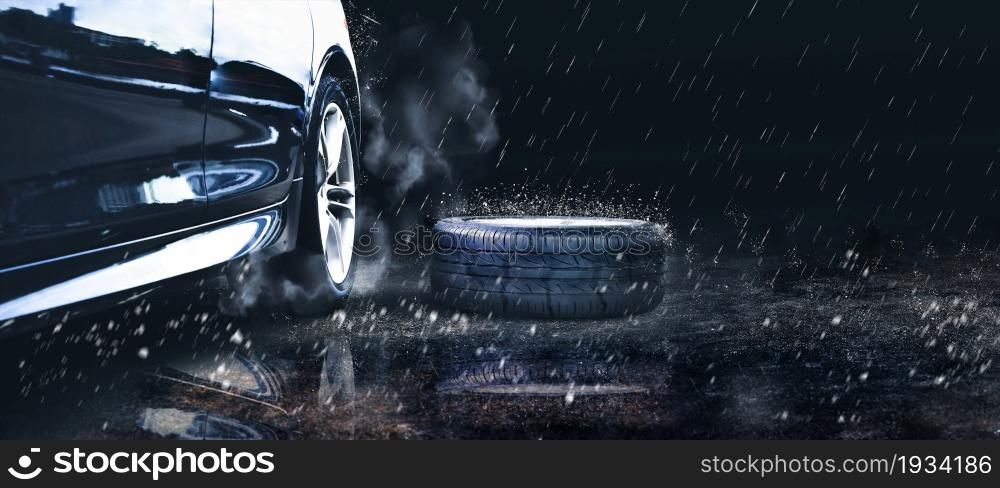 The black car spare wheel is placed on the road in the downpour, copy space on black background
