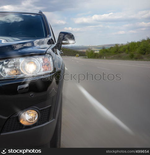 The black part of the car with a bumper and headlight on the background of an asphalt road