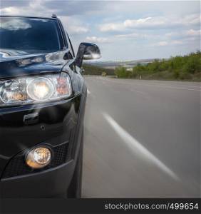 The black part of the car with a bumper and headlight on the background of an asphalt road