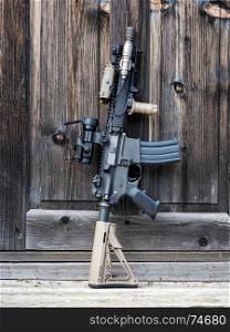 The Black Rifle. Tactical carbine beside wooden door of old house.