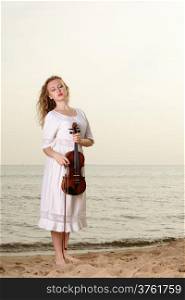 The blonde girl music lover on beach with a violin at sunset or sunrise. Love of music concept.