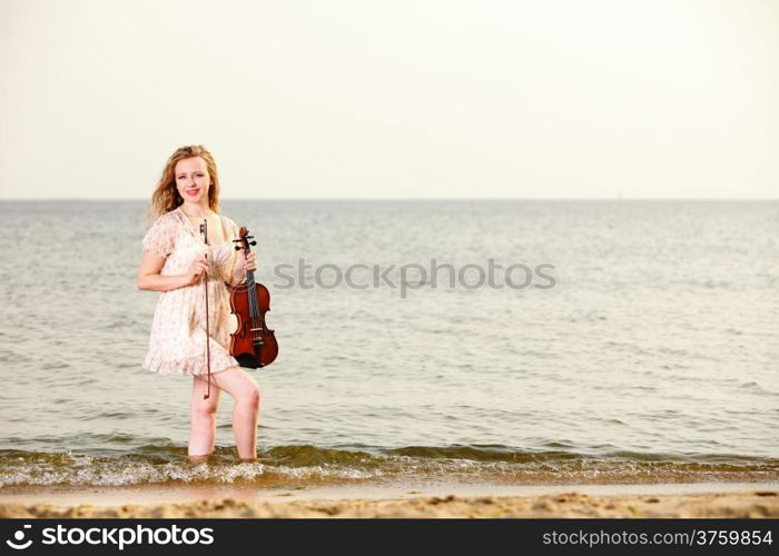 The blonde girl music lover on beach with a violin. Love of music concept.