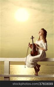 The blonde girl music lover on pier with a violin at sunset or sunrise. Love of music concept.