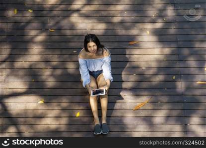 The blue shirt woman is sitting watching the text on the tablet while sitting in the park from a high angle.