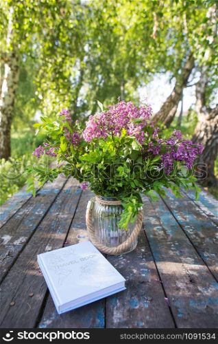 The book, a beautiful bouquet of lilacs is on an old table. Close-up.. The book, a beautiful bouquet of lilacs is on an old table. Close-up