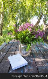 The book, a beautiful bouquet of lilacs is on an old table. Close-up.. The book, a beautiful bouquet of lilacs is on an old table. Close-up