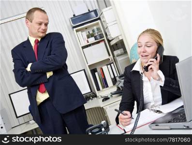The boss walking in on a secretary and looking commiserating who is chatting on the phone with a friend, not tending to business.