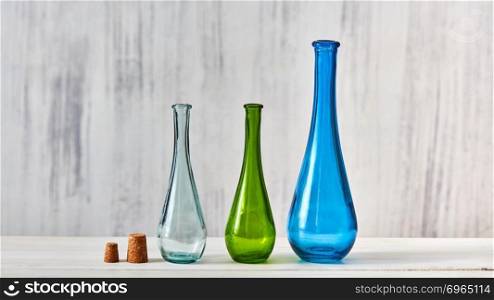 The bottles green, blue, transparent stand on a gray table on a light gray background with place for text. Concept of saving homemade products.. Three colorful glass bottles different sizes for saving natural olive oil on a gray background, a table