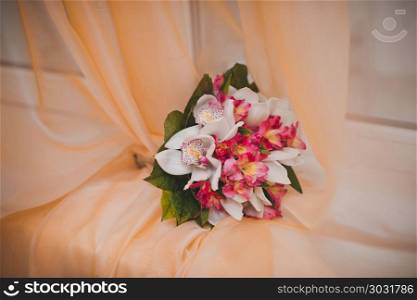 The bouquet for the bride lies on an orange curtain on a window sill.. Bouquet on a window sill.