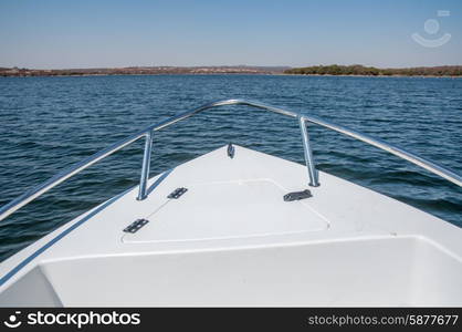 The bow of a boat moving over the water of a dam, with the land vissible as the horizon.