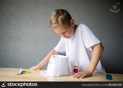The boy cuts out details from paper. Glue the parts together with glue.. The boy cuts out details from paper. Glue the parts together with glue