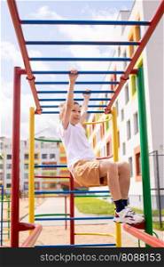 The boy does sports on horizontal bars of different colors. A teenage boy is engaged on horizontal bars near the school