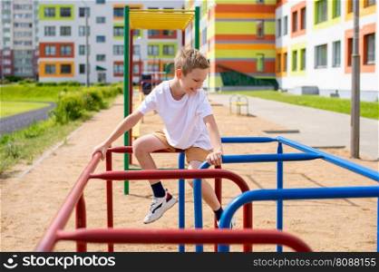 The boy does sports on horizontal bars of different colors. A teenage boy is engaged on horizontal bars near the school