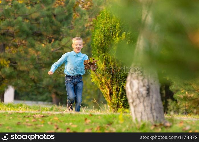 The boy happily runs through the park on the green grass