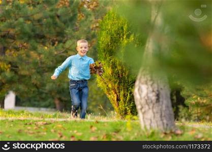 The boy happily runs through the park on the green grass