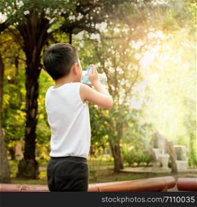 The boy is drinking water from a plastic bottle after exercising While the sun is falling, there is light passing through the trees.