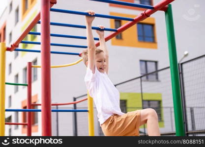 The boy plays sports on the horizontal bars . Arm strength. A teenage boy is engaged on horizontal bars near the school