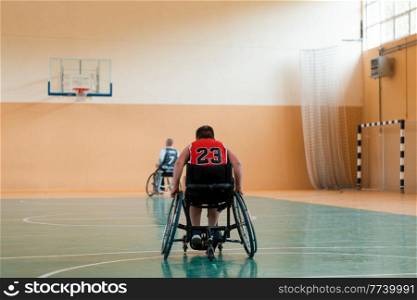the boy sits in a wheelchair and prepares for the basketball start of the game in the big arena. Selective focus . the boy sits in a wheelchair and prepares for the basketball start of the game in the big arena
