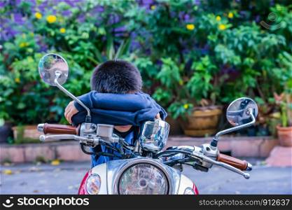 The boy sitting and sleeping on the motorcycle.