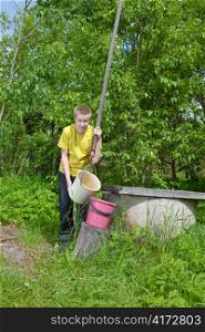 The boy, the teenager, pours water in a bucket from a well