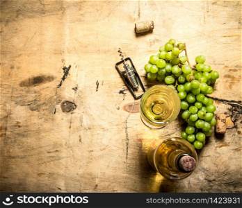 The branch of grapes with a bottle of white wine . On wooden background.. The branch grapes with a bottle white wine .