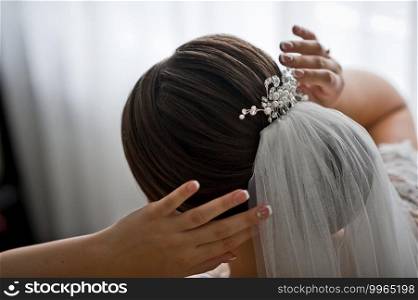 The bride adjusts the wedding veil and pearl jewelry in her hair.. A beautiful wedding decoration for the brides hairstyle made of natural s