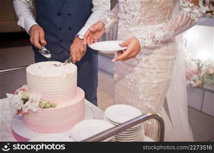The bride and groom are cutting the wedding cake into pieces.. The bride and groom divide the wedding cake into parts for the guests 42