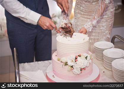 The bride and groom are cutting the wedding cake into pieces.. The bride and groom divide the wedding cake into parts for the guests 42
