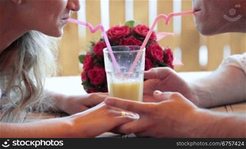 the bride and groom drink orange juice from one glass at a cafe
