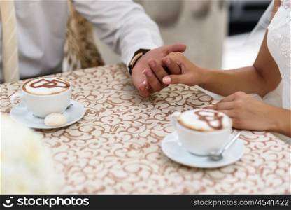 the bride and groom holding hands, sitting in a cafe at a table with coffee