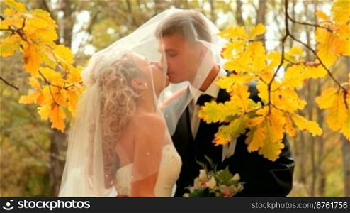 the bride and groom kissing in the autumn park