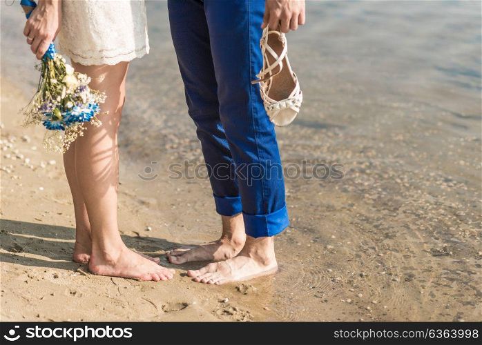 the bride and groom standing barefoot on the banks of the river, the bride holds wedding bouquet with blue flowers
