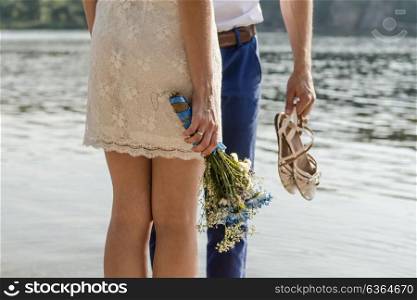 the bride and groom standing barefoot on the banks of the river, the bride holds wedding bouquet with blue flowers