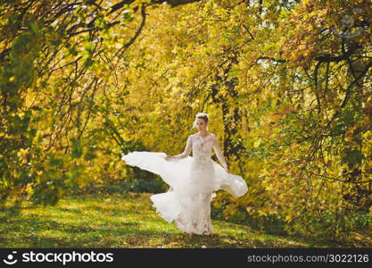 The bride happily spinning in the developing dress on the edge of the bright autumn forest.. Portrait of a bride in a white dress swirling in the meadow autumn forest