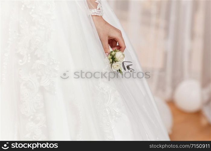 The bride holding in hand the groom&rsquo;s buttonhole flowers with white roses, and green and greenery. Bride&rsquo;s Preparations. Wedding Morning concept.