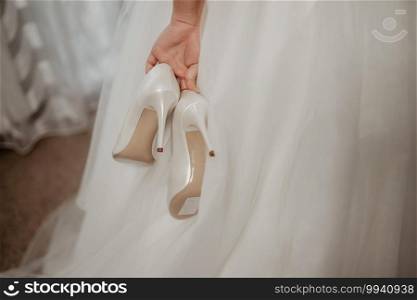 The bride holds a pair of white shoes. A pair of bridesmaid shoes.. bride holds a pair of white shoes. A pair of bridesmaid shoes.