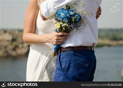 the bride hugs the groom and holds a Bridal bouquet with blue flowers on a background of the river