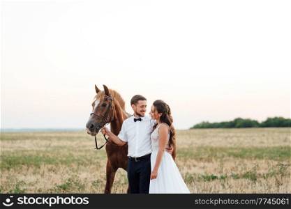 the bride in a white dress and the groom in a white shirt on a walk with brown horses