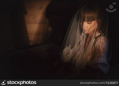 The bride in sexy underwear or night dress from the veil on her head is sitting in the room on the armchair at home. Preparing for a wedding in the morning.