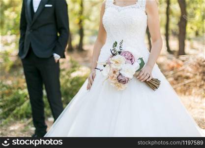the bride in the white dress, groom standing behind her and a bunch of flowers in her hand