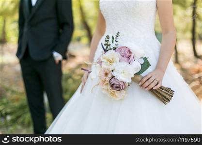 the bride in the white dress, groom standing behind her and a bunch of flowers in her hand