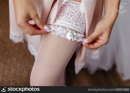 The bride in white puts on a beautiful openwork bandage on an elegant leg. Wedding concept.. The bride in white puts on a beautiful openwork bandage on an elegant leg. Wedding concept