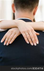 The bride&rsquo;s hands with an engagement ring on her finger embrace the groom by the neck