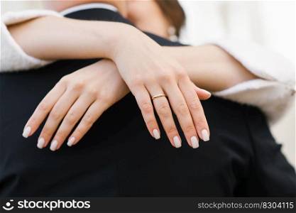 The bride’s hands with an engagement ring on her finger embrace the groom by the neck