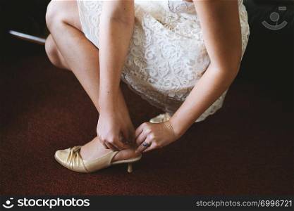The bride with wedding dress is getting ready putting on shoes