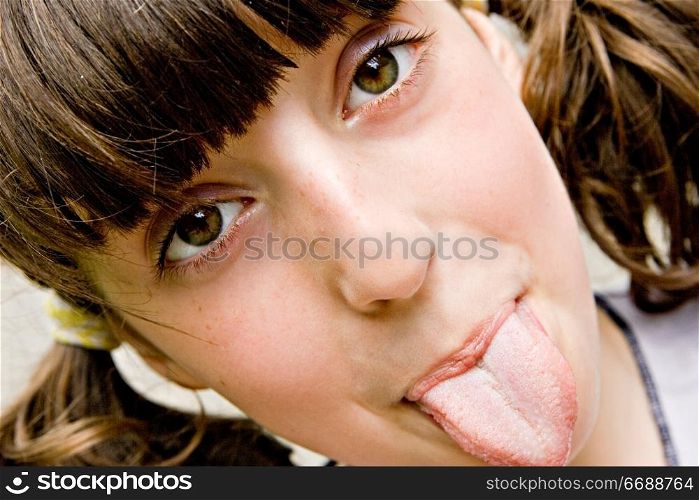 The brown-eyed dark-haired girl-teenager looks directly in a shot and puts out the tongue