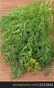 The bunch of dill with flower, lying on wicker to a mat on kitchen