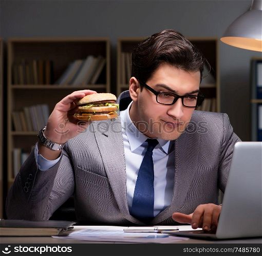 The businessman late at night eating a burger. Businessman late at night eating a burger