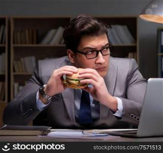 The businessman late at night eating a burger. Businessman late at night eating a burger